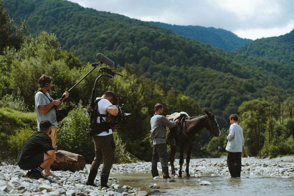 Film crew prepares horse while filming in a scenic mountainous valley setting.